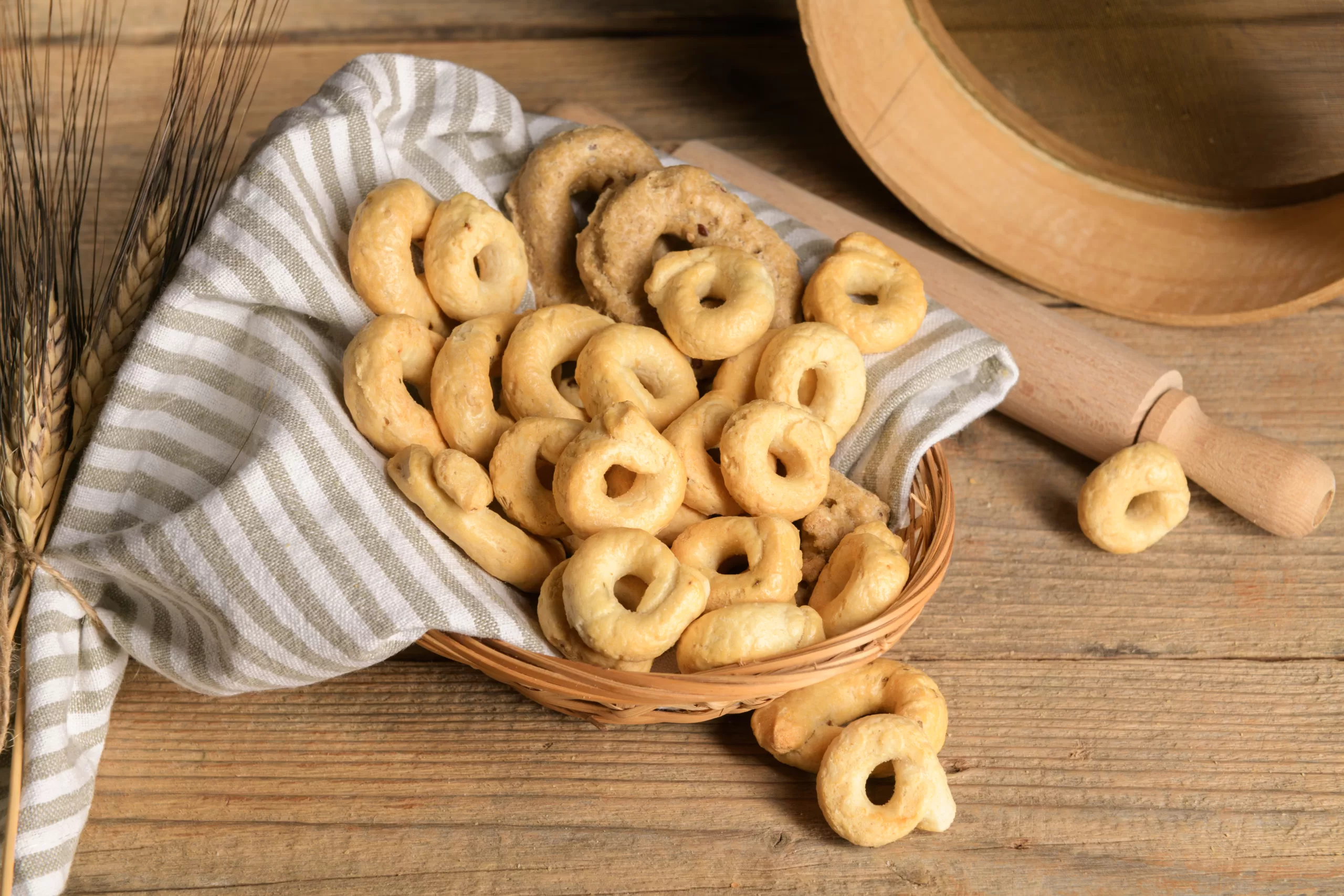 A basket overflowing with homemade tarallis resting on a wooden table.