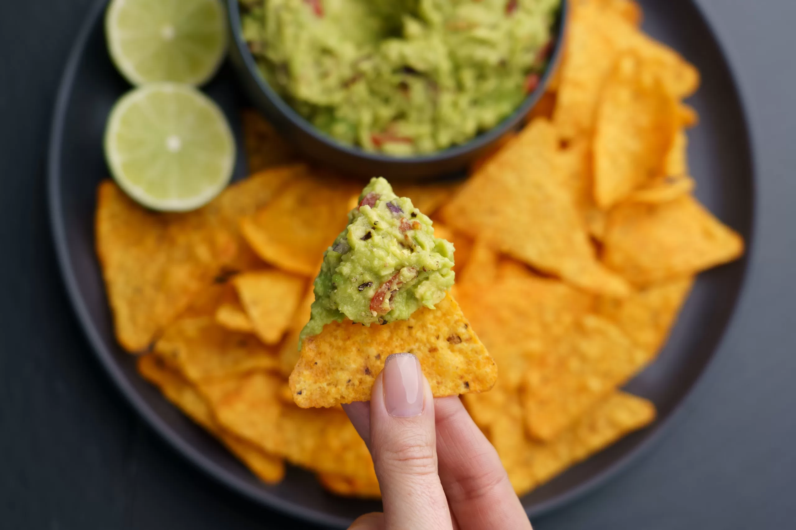  Top view of a woman's hand holding tortilla chips with tasty guacamole sauce.