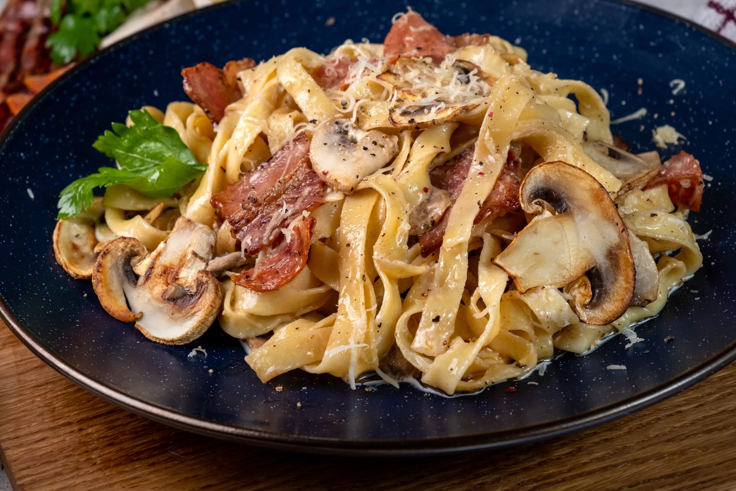 Tagliatelle in creamy sauce with mushrooms and parmesan served on a black plate.