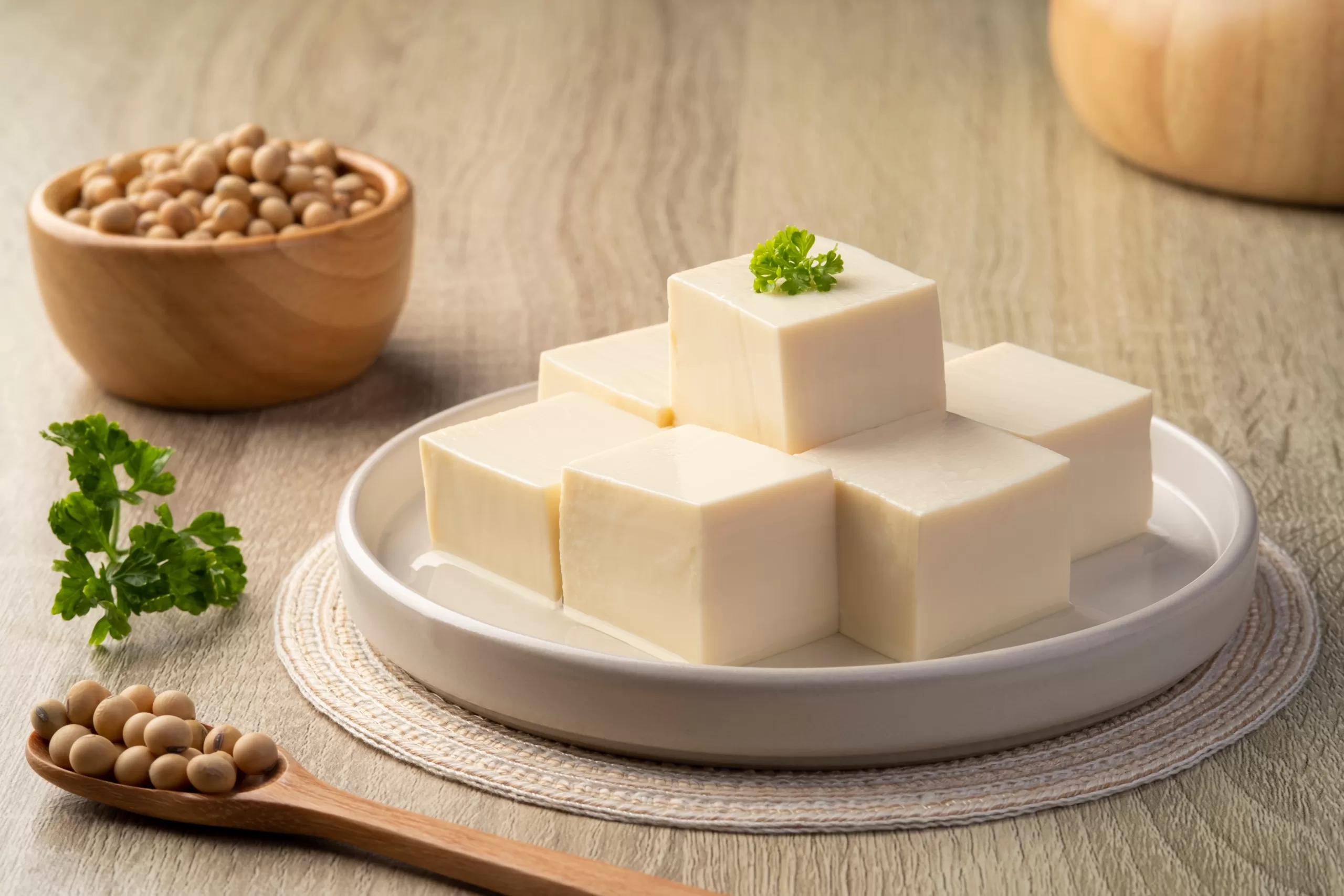 Tofu cubes stacked on a ceramic plate, and soy beans nearby. 
