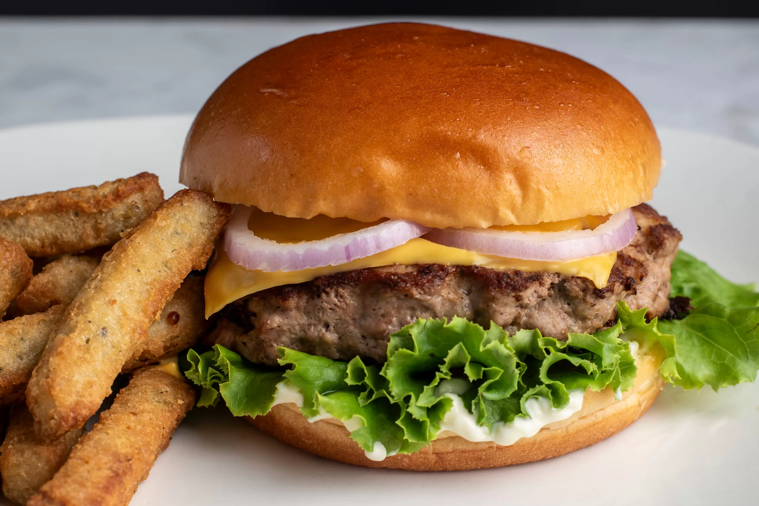 A turkey burger with cheese and onions on a brioche bun, accompanied by broccoli fried sticks.