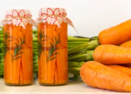 Two jars of pickled carrots in front of a bundle of fresh carrots.