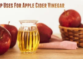 A wooden table displaying a vessel of apple cider vinegar and a basket overflowing with fresh apples. The text reads, "X Top Uses For Apple Cider Vinegar."
