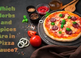 A black countertop displaying all the ingredients for pizza, including herbs and spices. The text reads, "Which Herbs and Spices Are in Pizza Sauce?"