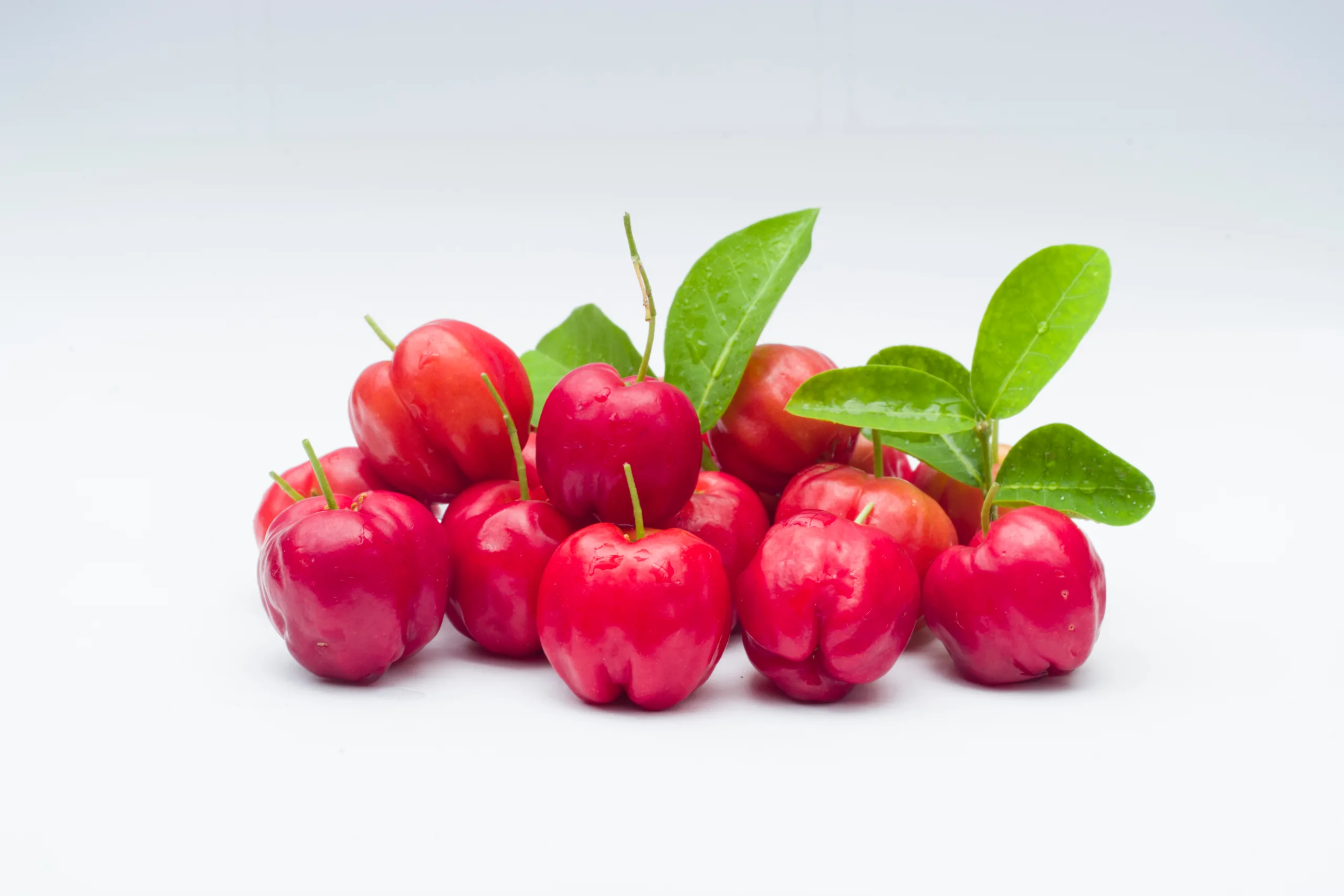A handful of West Indian cherries on a white background.