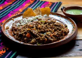 Plate with refried beans, crumbled cheese, and meat, tortilla chips and green sauce on side.