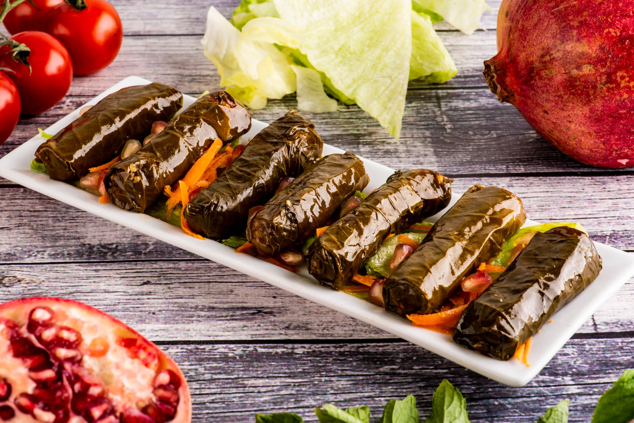 A tray full of warak enab rolls on a weathered wooden table.