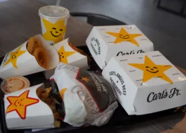 Carl's Jr. meal with burger, fries, onion rings, and drink on a tray.