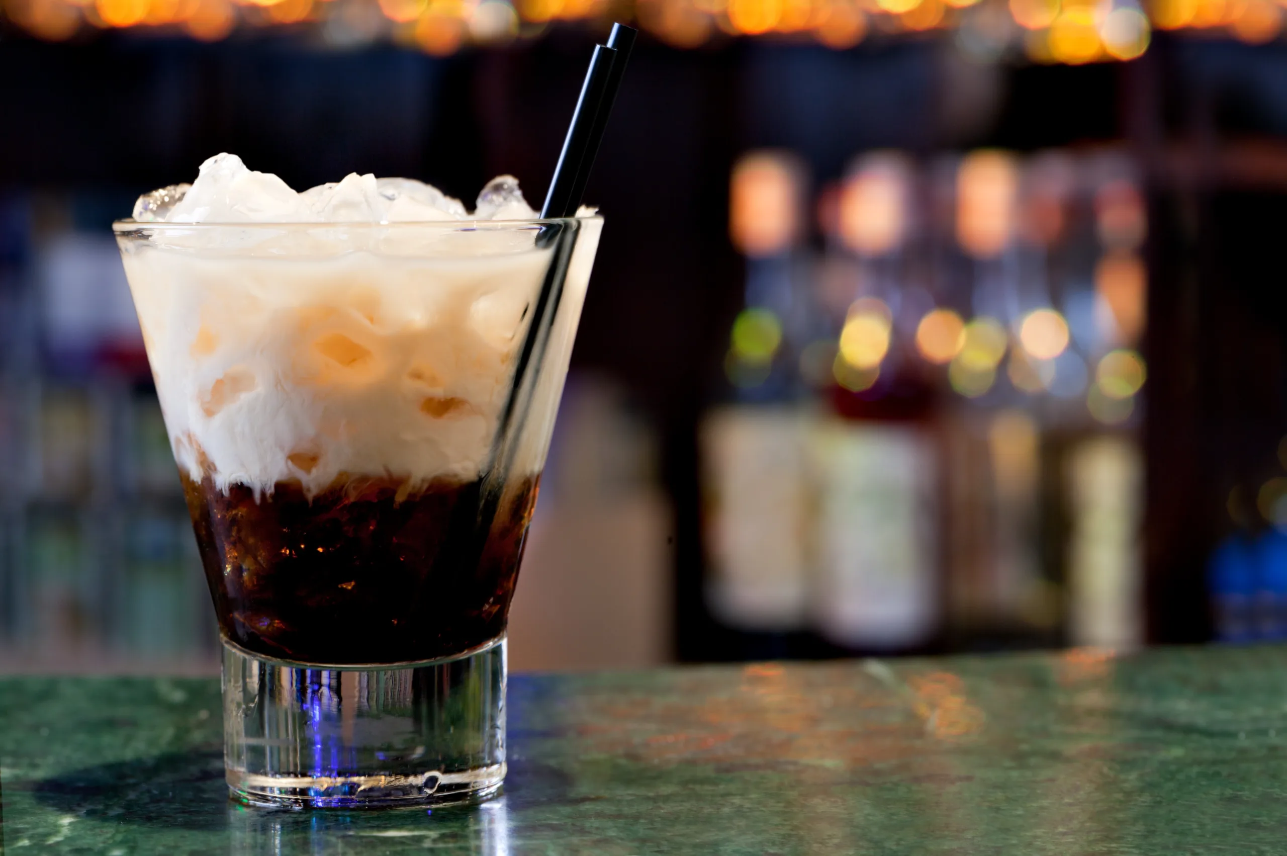 A bar countertop featuring a glass of white Russian cocktail.