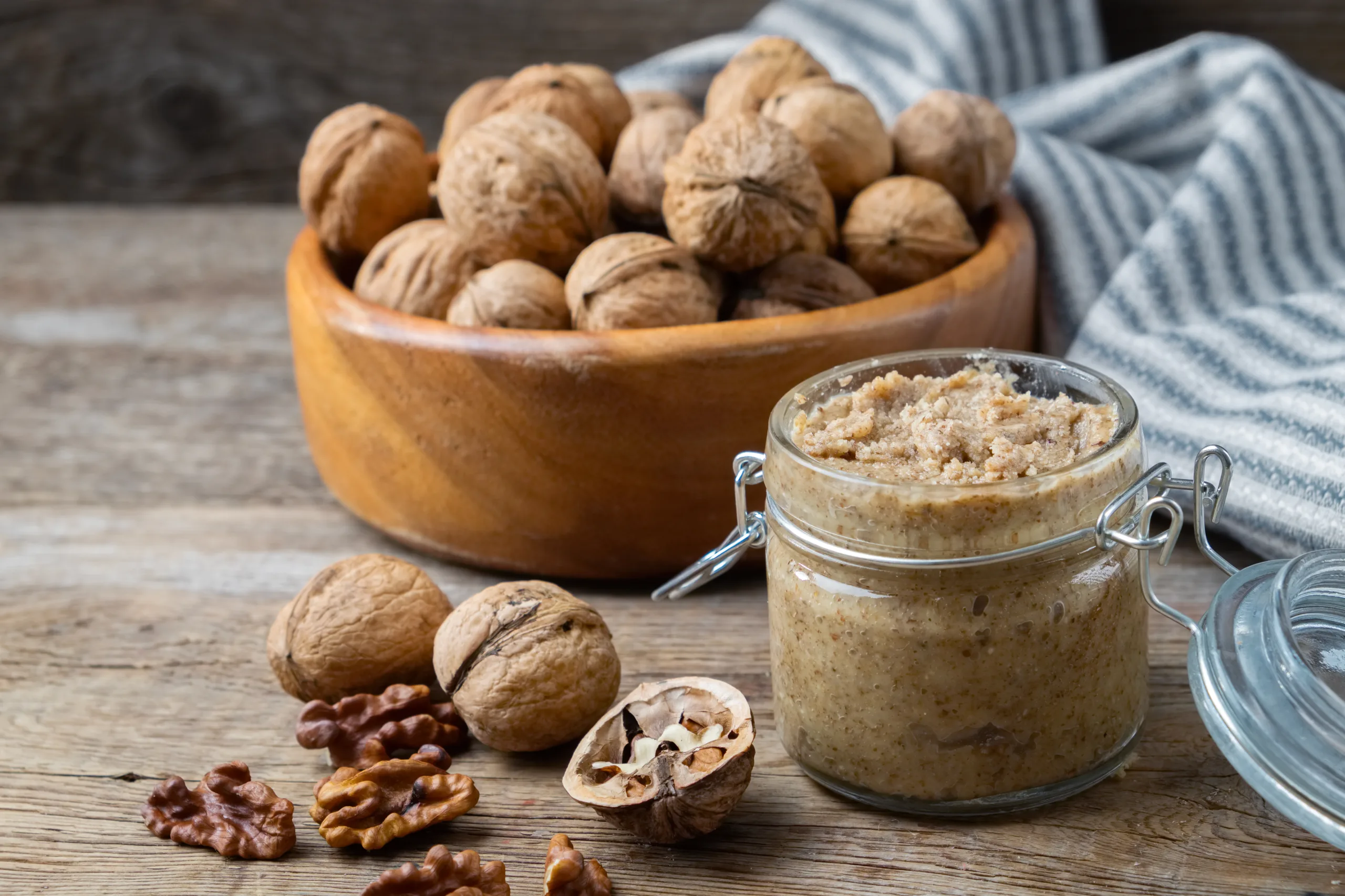 A wooden table showing a jar of walnut butter, accompanied by fresh walnuts.