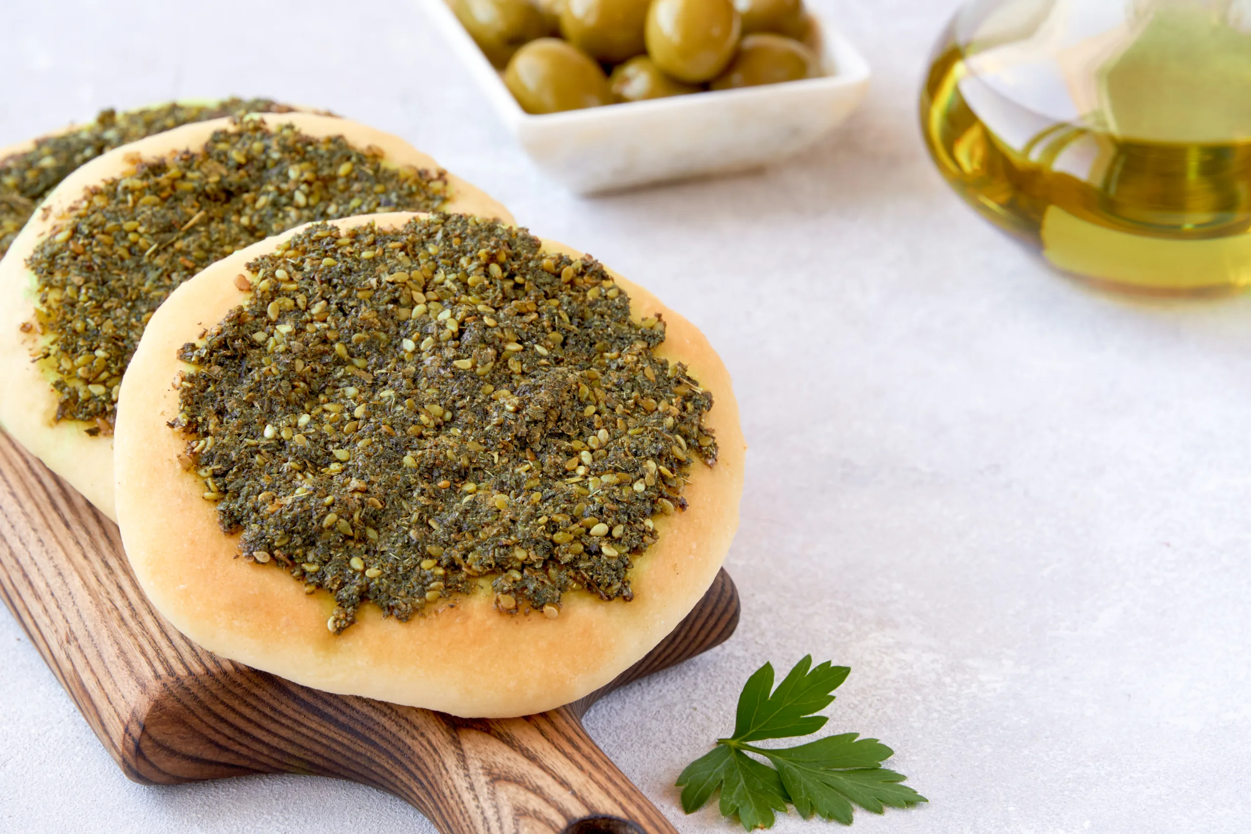 A concrete table featuring a few zaatar bread pieces, olives, and olive oil. 