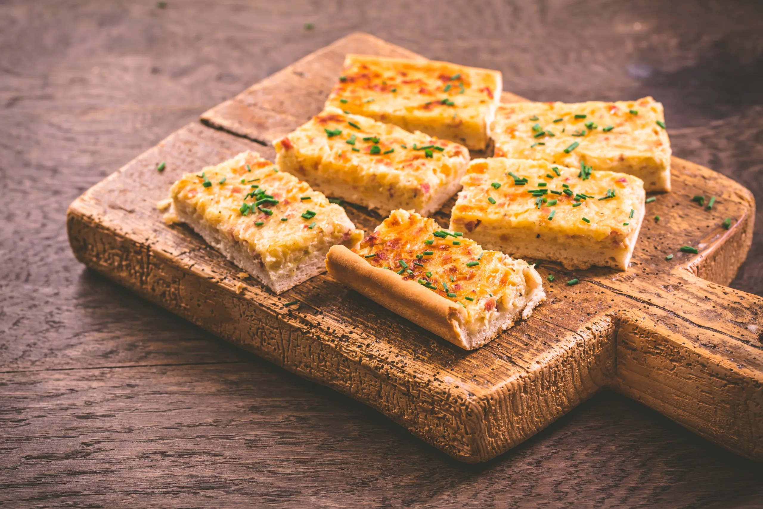 A vintage chopping board featuring some pieces of zwiebelkuchen.