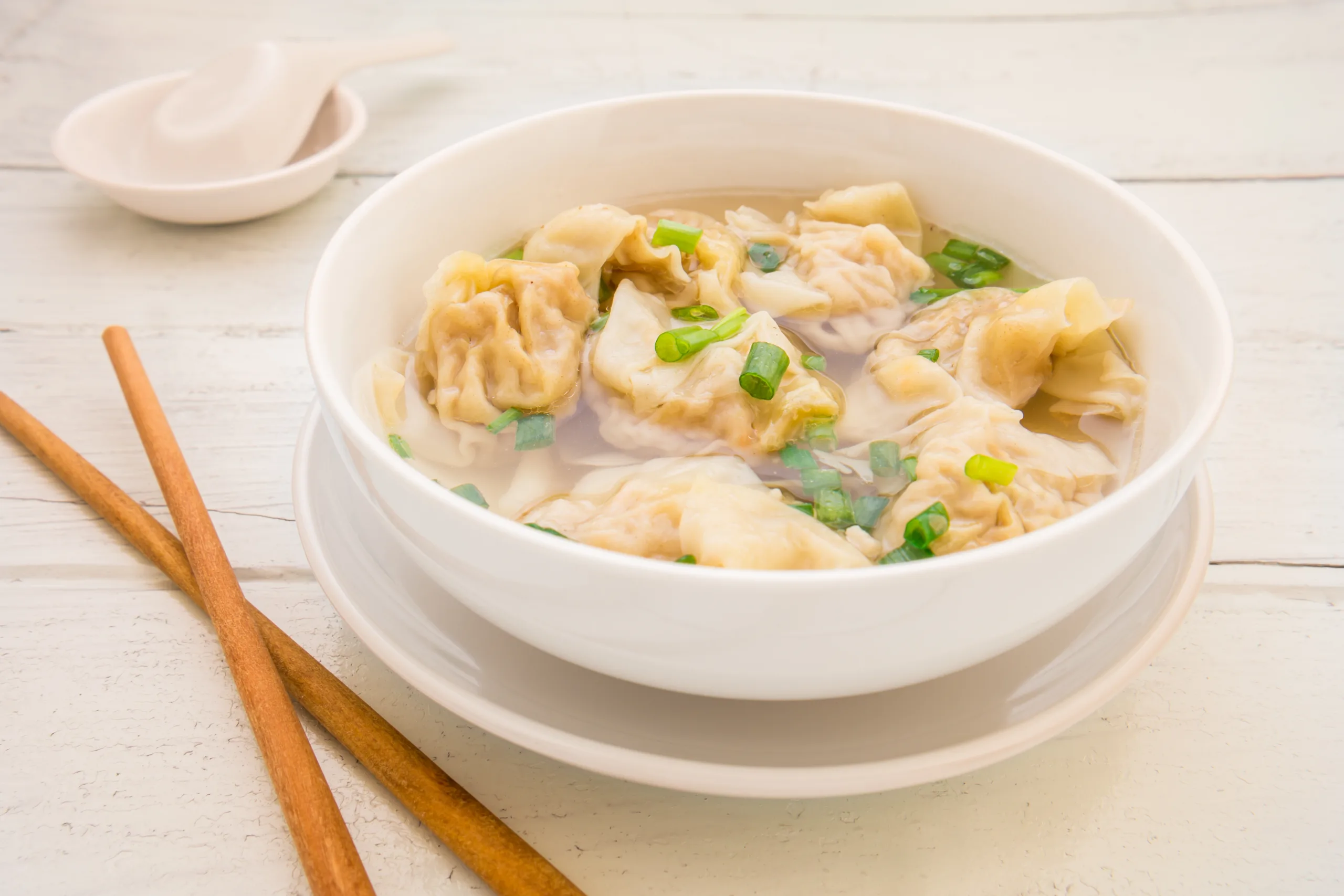 A white wooden table showcasing a portion of wonton soup.