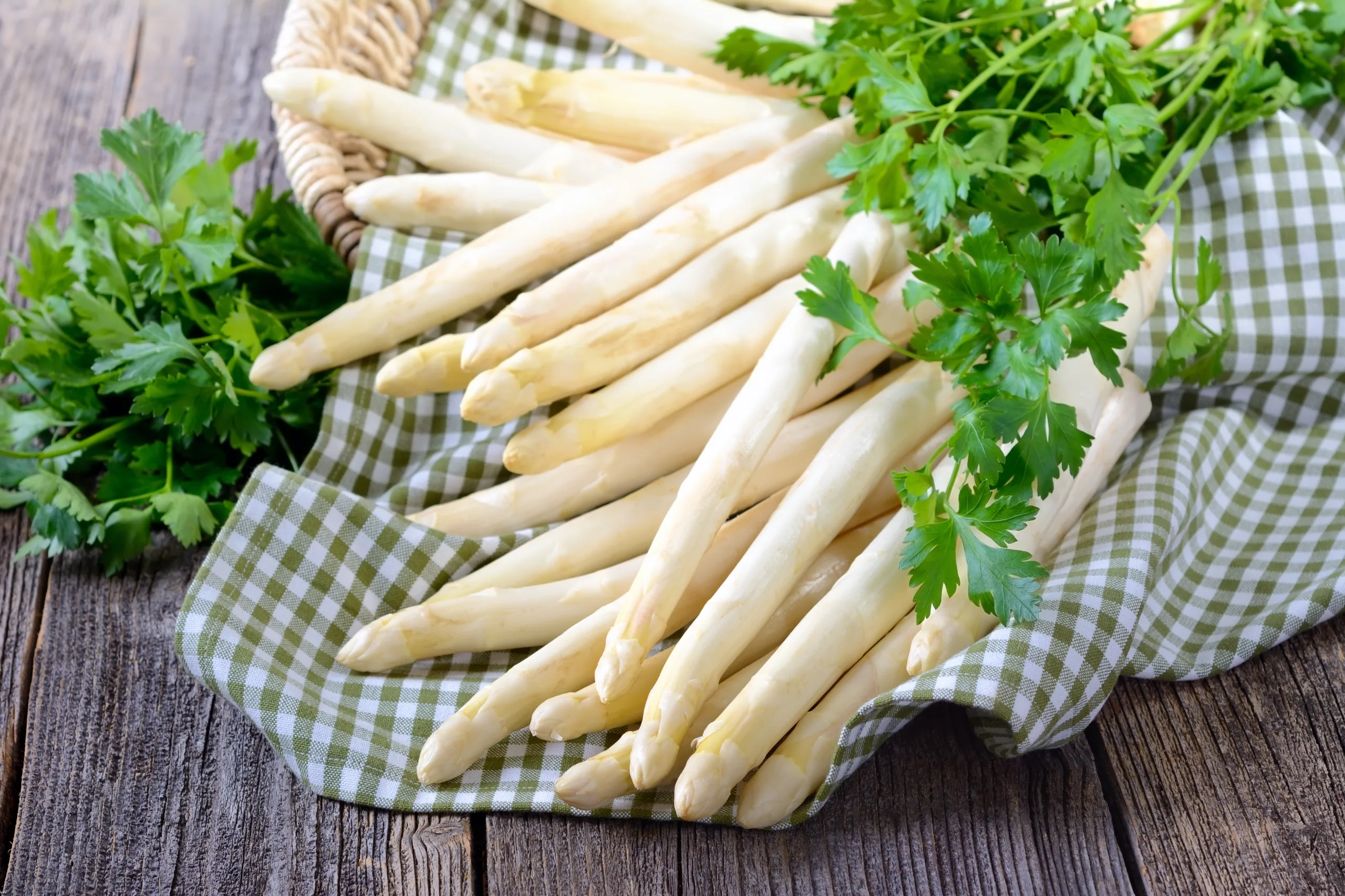 White asparagus and parsley leaves on a rustic wooden table.