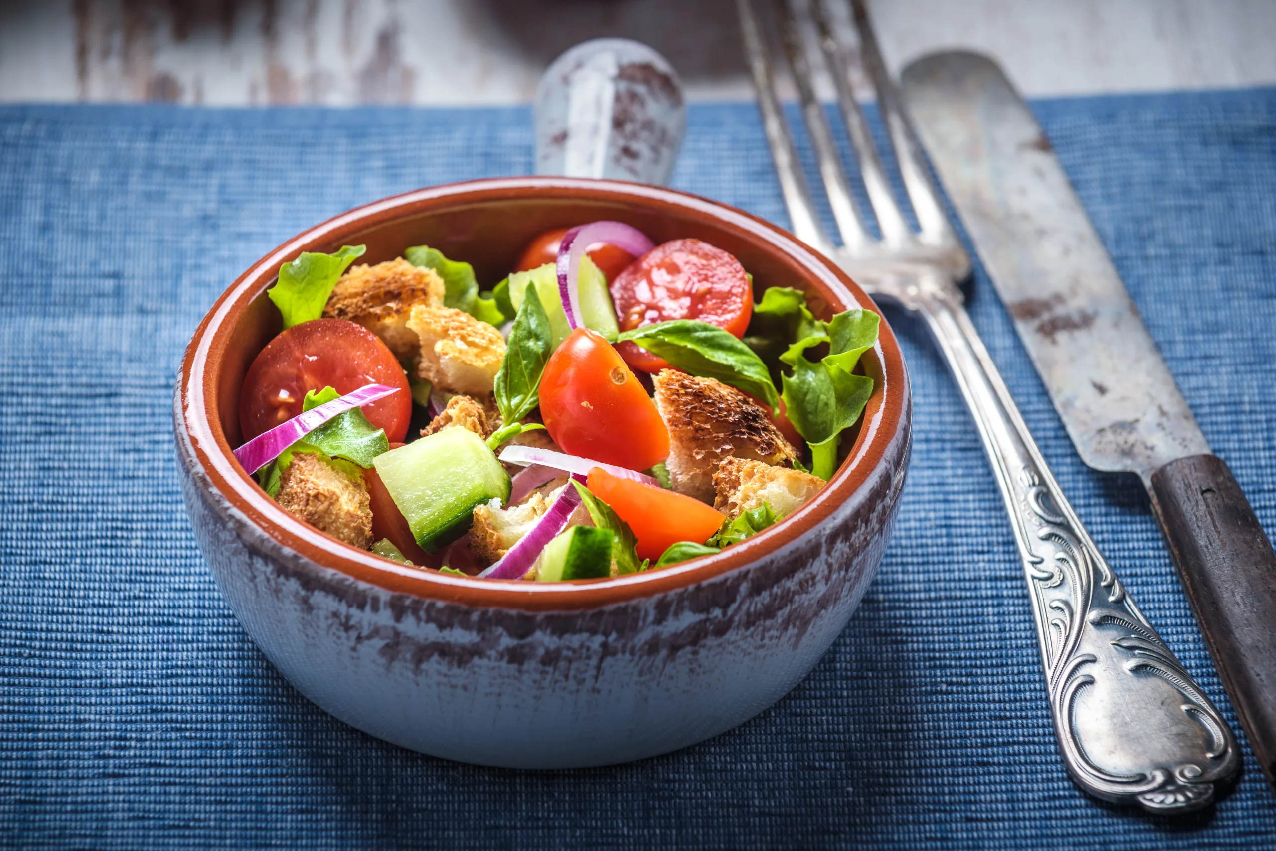 A blue table mat holding a zanella full of panzanella. 