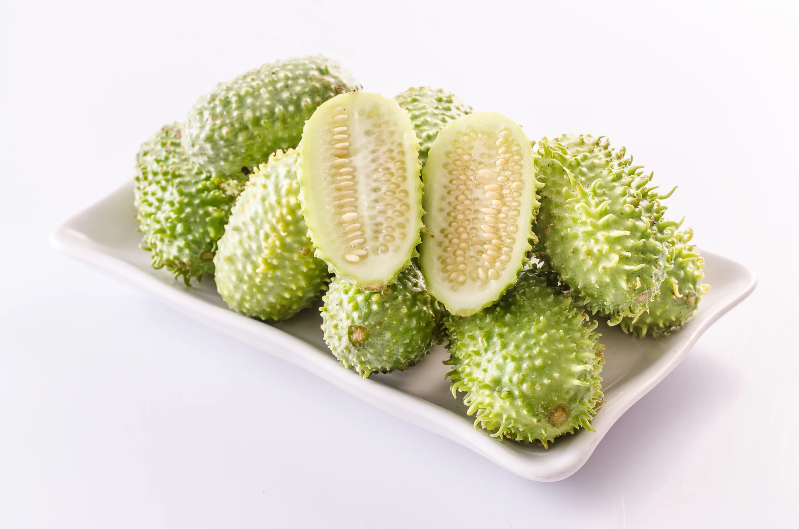 A white background featuring a tray piled high with fresh West Indian gherkins.