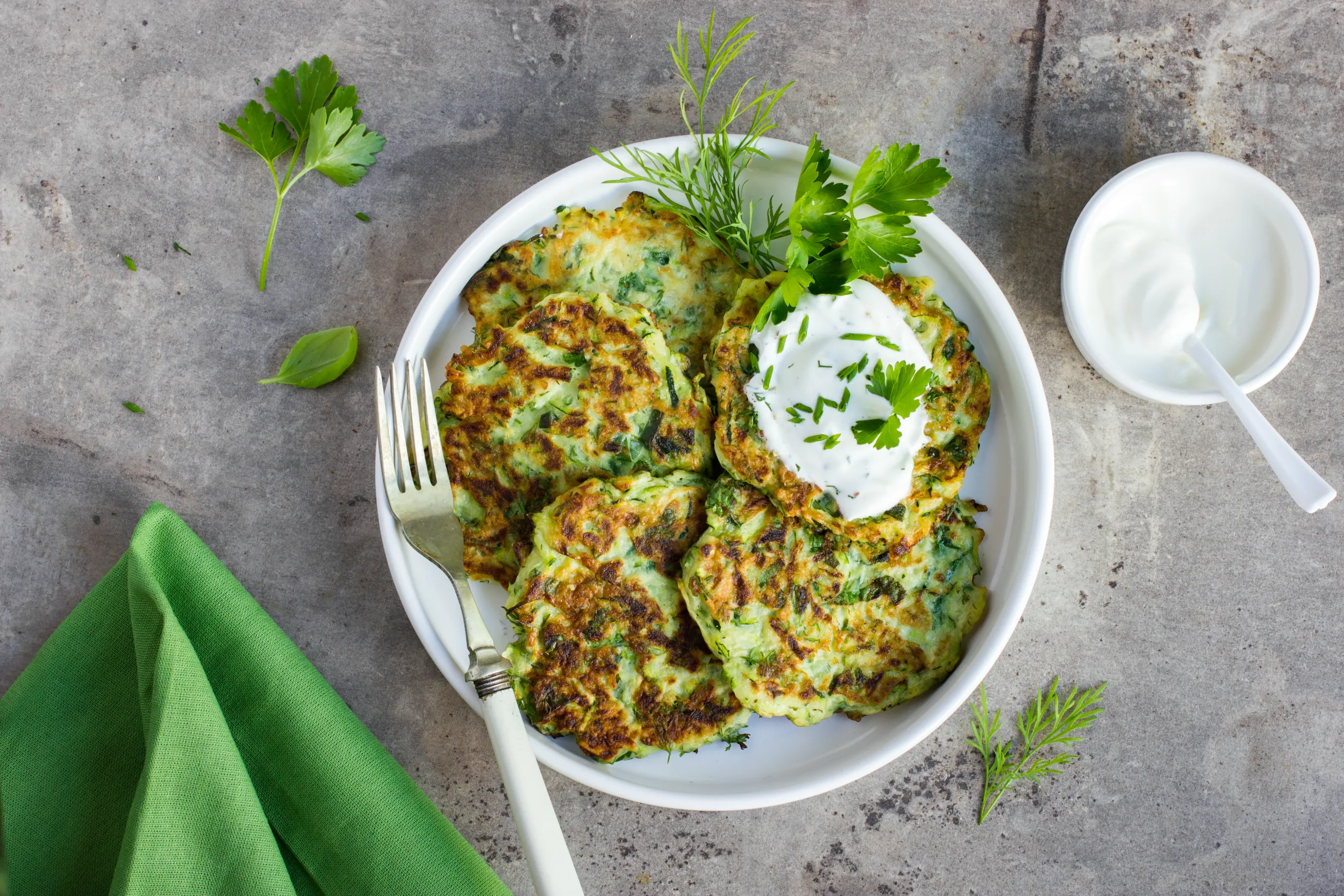 A concrete surface showing zucchini fritters with yogurt dill sauce.
