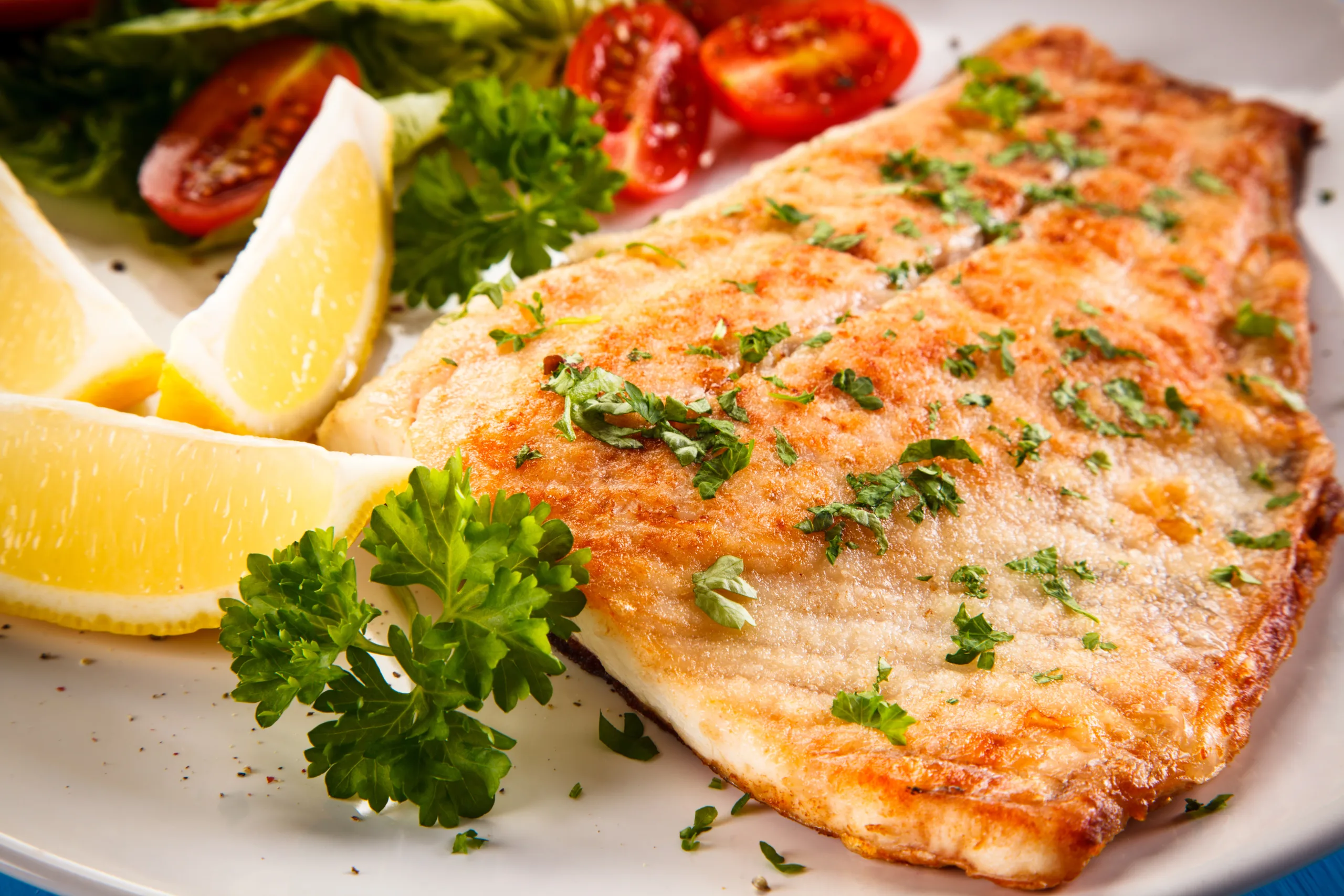 A portion of grilled white flounder with vegetables and lemon.