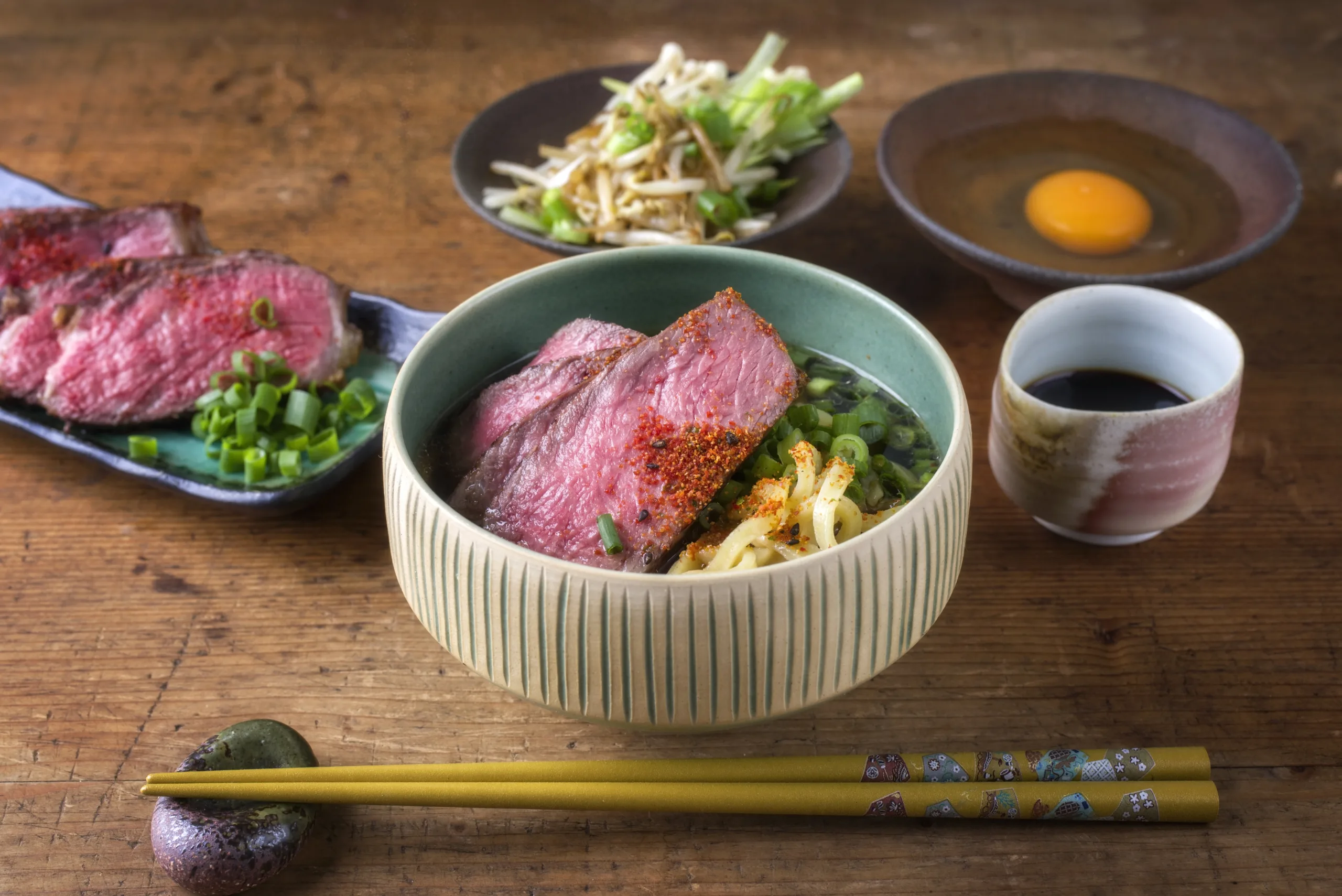 A wooden table served with ramen and waygu beef.