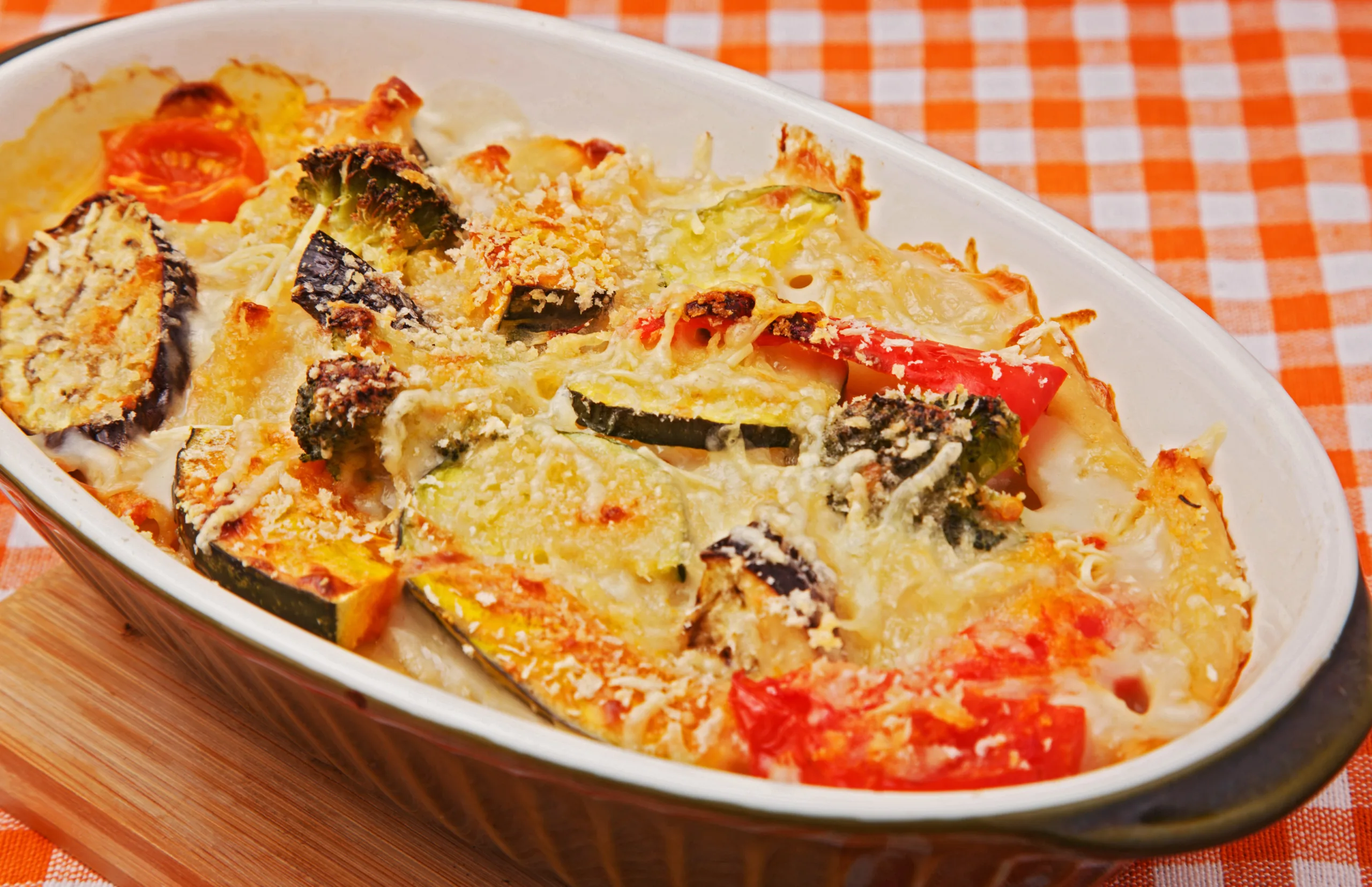 A platter full of zucchini tomato gratin resting on a checkered table mat.