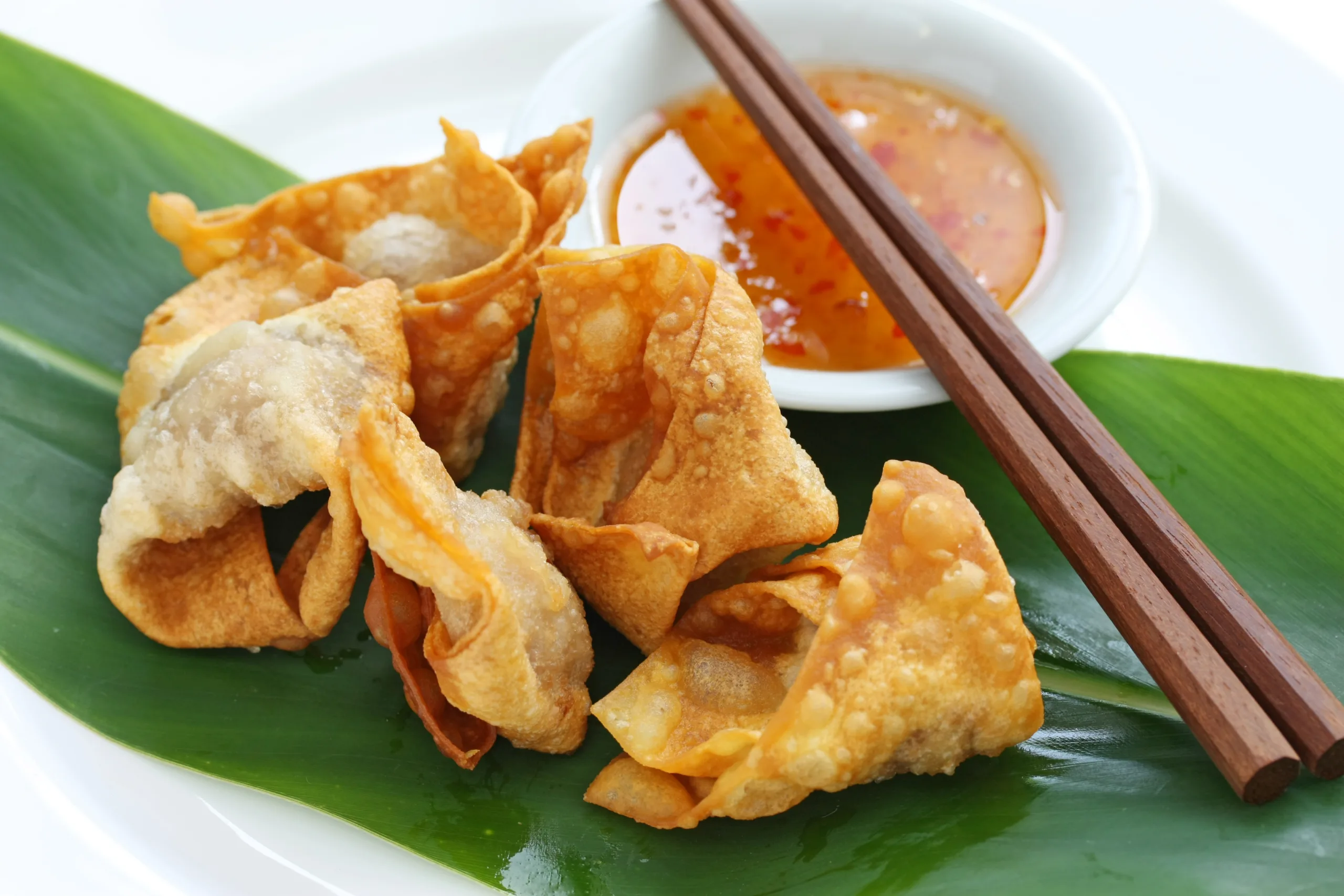 A few fried wonton dumplings on a green leaf.