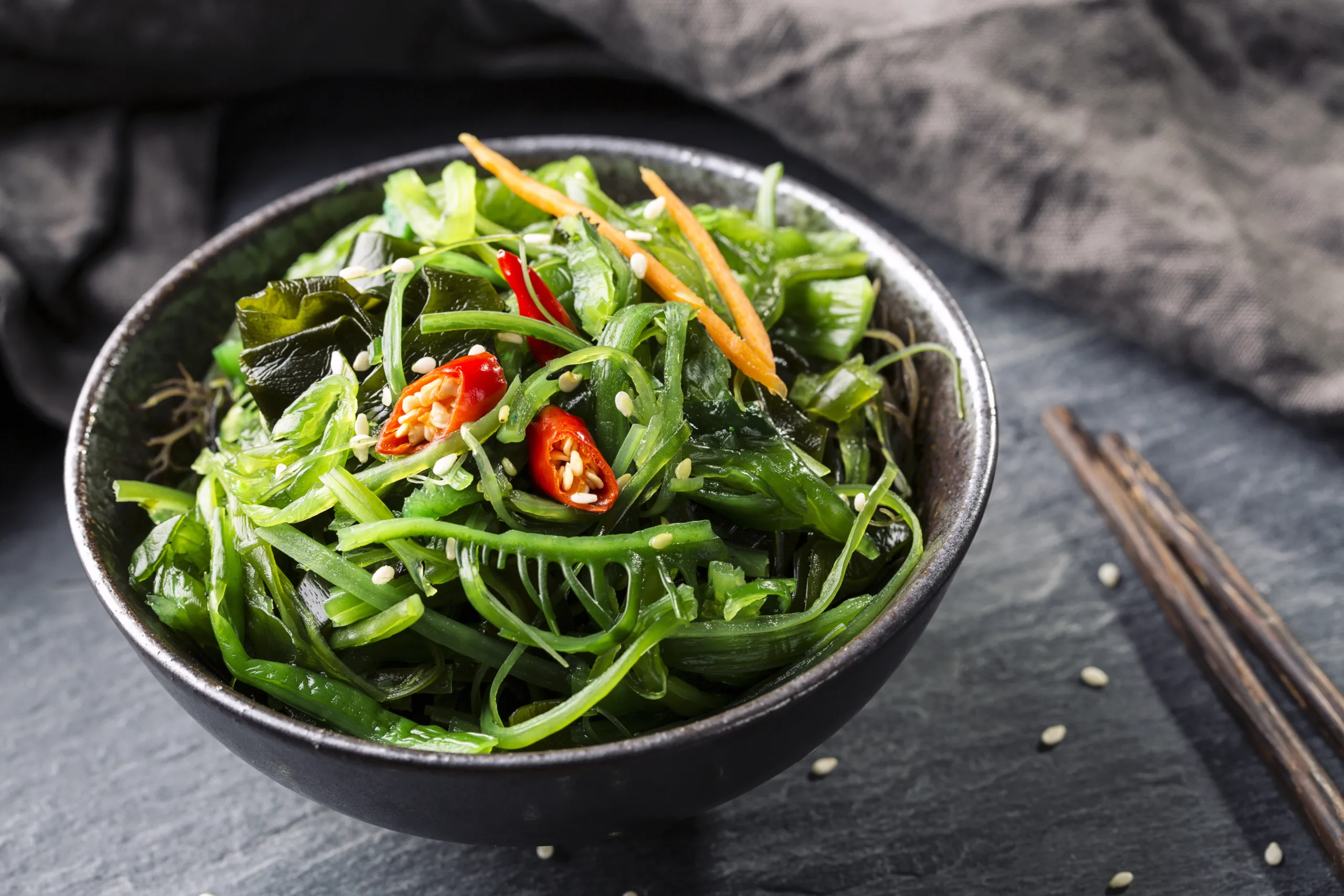 A concrete table featuring a bowl full of wakame seaweed salad.
