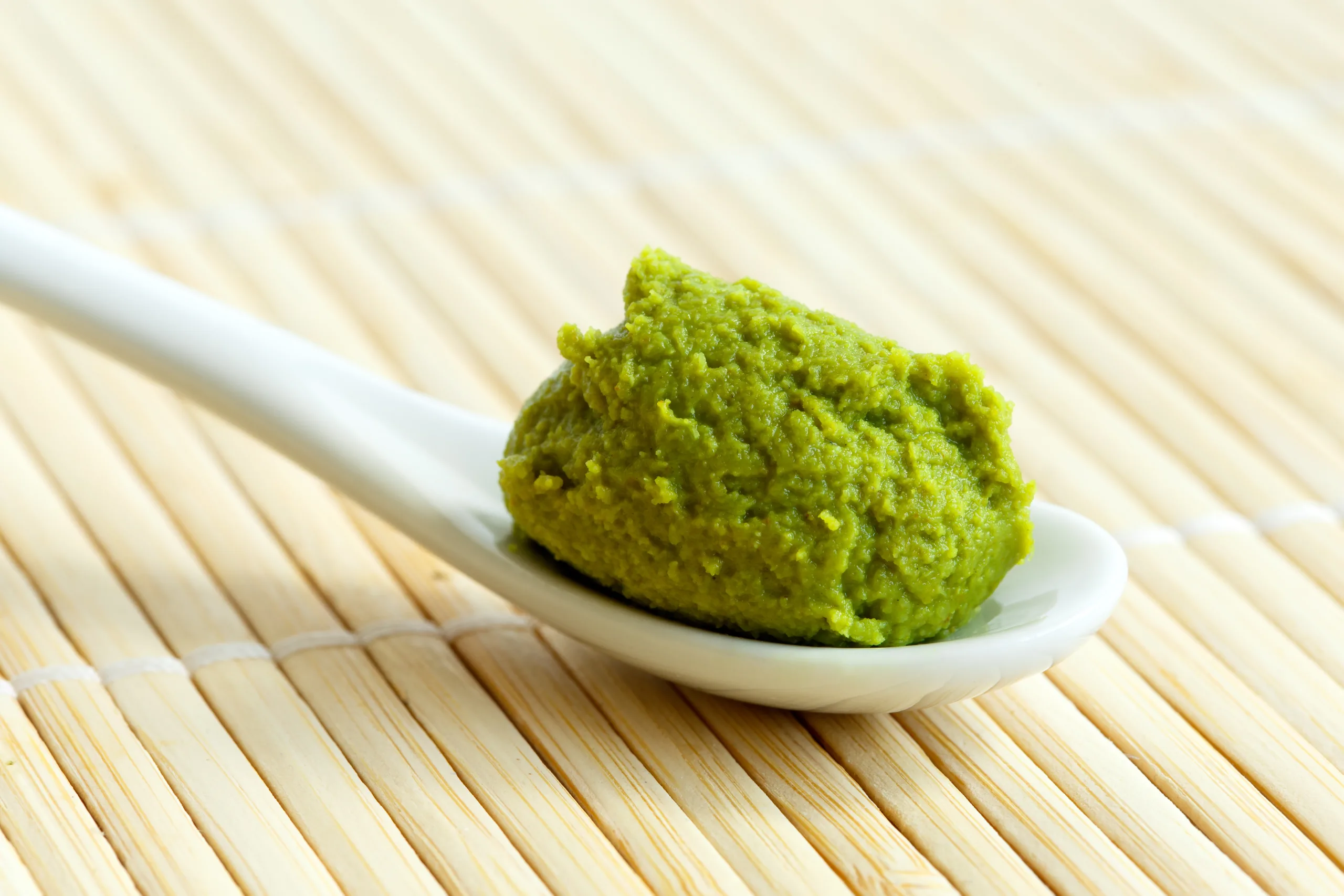 A spoon heaped with wasabi paste sitting on a bamboo platemate.
