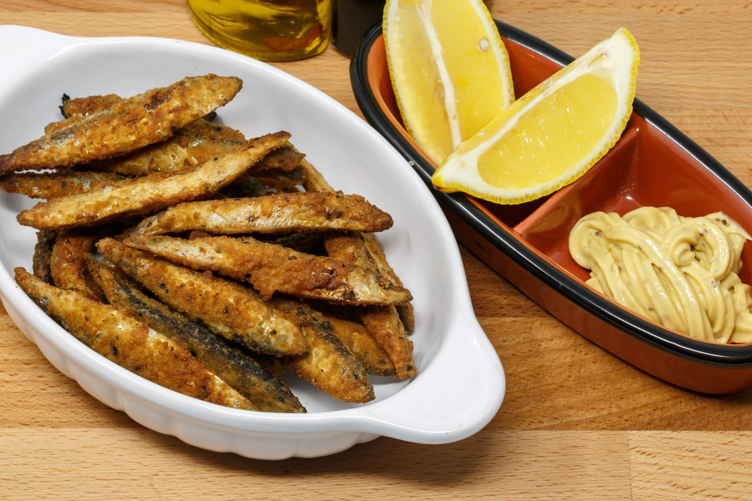 A platter full of fried white bait with mayonnaise and lemon.