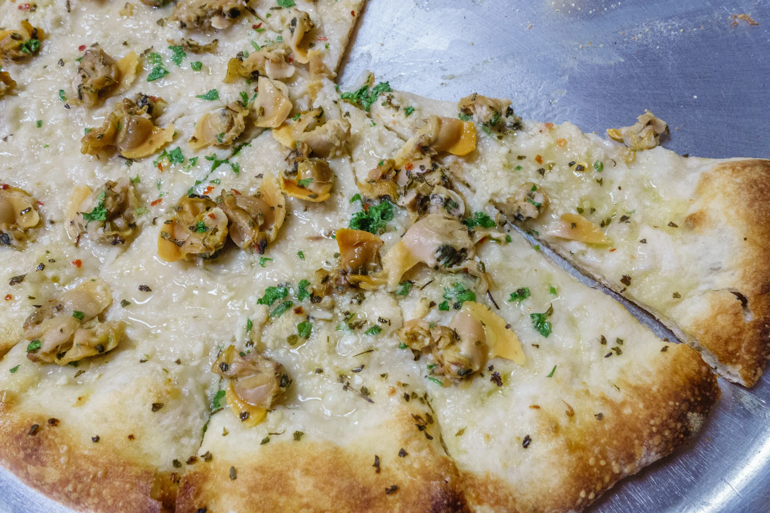 A partially cut white clam pizza.