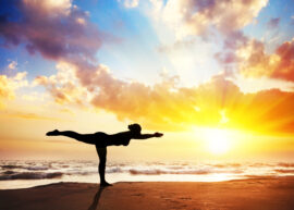 Woman doing a warrior pose in silhouette with sunset sky background.