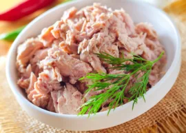 White bowl filled with shredded tuna and dill sprigs on burlap.