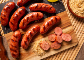Grilled sausages with grill marks, sliced sausage pieces, and breadcrumbs on a wooden board.