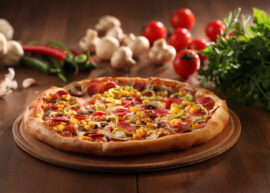 Whole Italian pizza surrounded by garlic cloves, tomatoes, and peppers