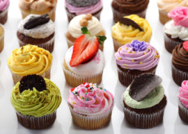 Variety of cupcakes with colorful frosting and toppings on a white surface.