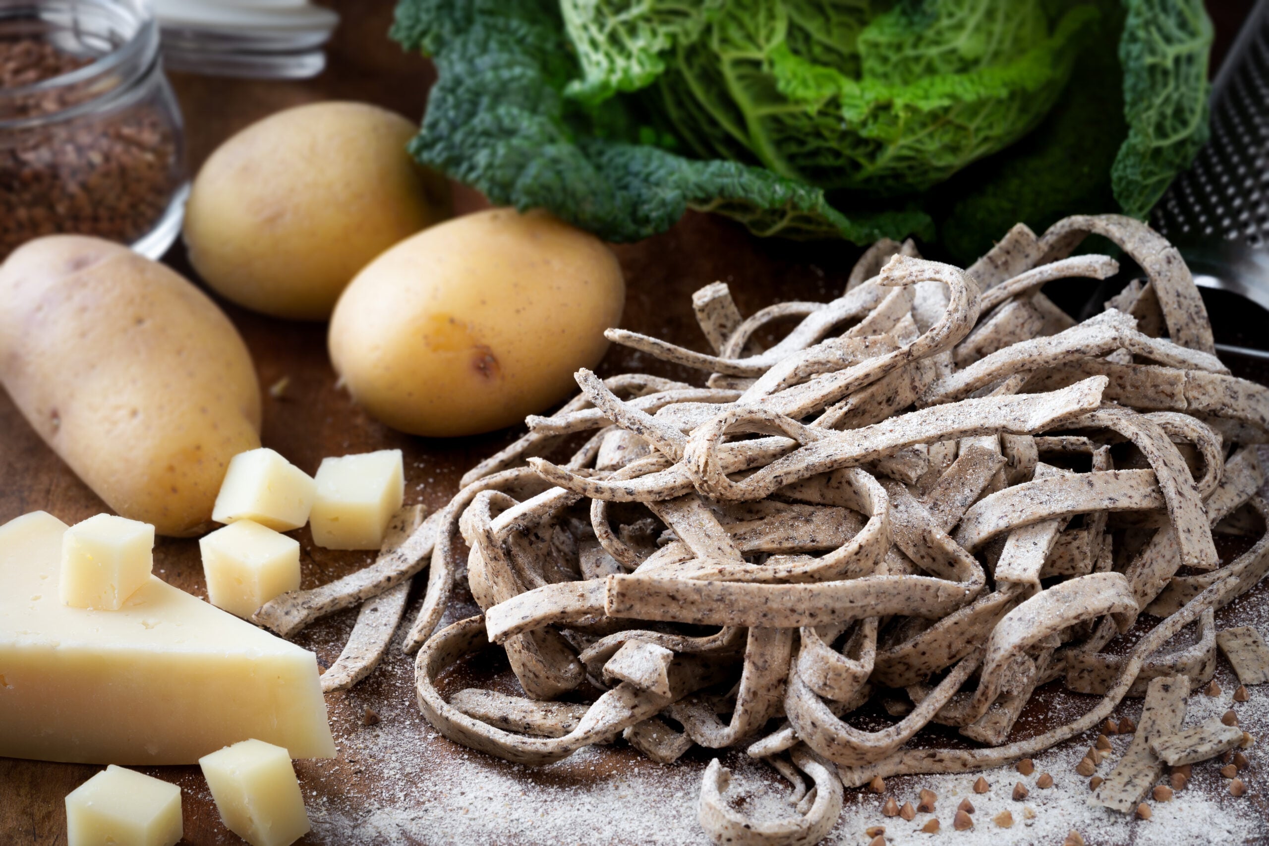 All the ingredients to prepare pizzoccheri alla Valtellinese displayed in a wooden table. 