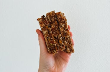 A hand holding a stack of three almond flour trail bars in front of a white wall.