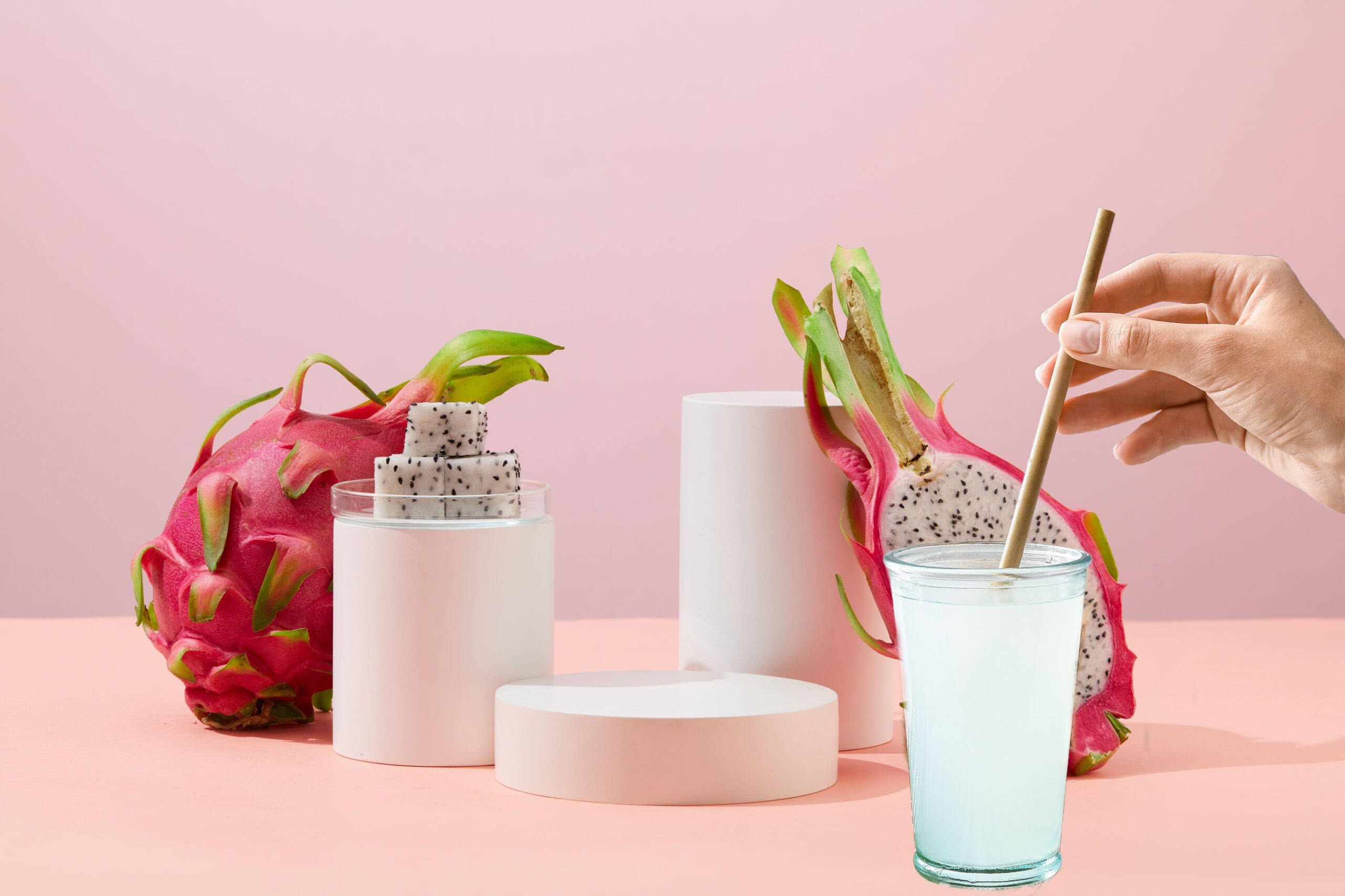 A person stirring a dragonfruit agua fresca, accompanied by a few fresh dragon fruits. 