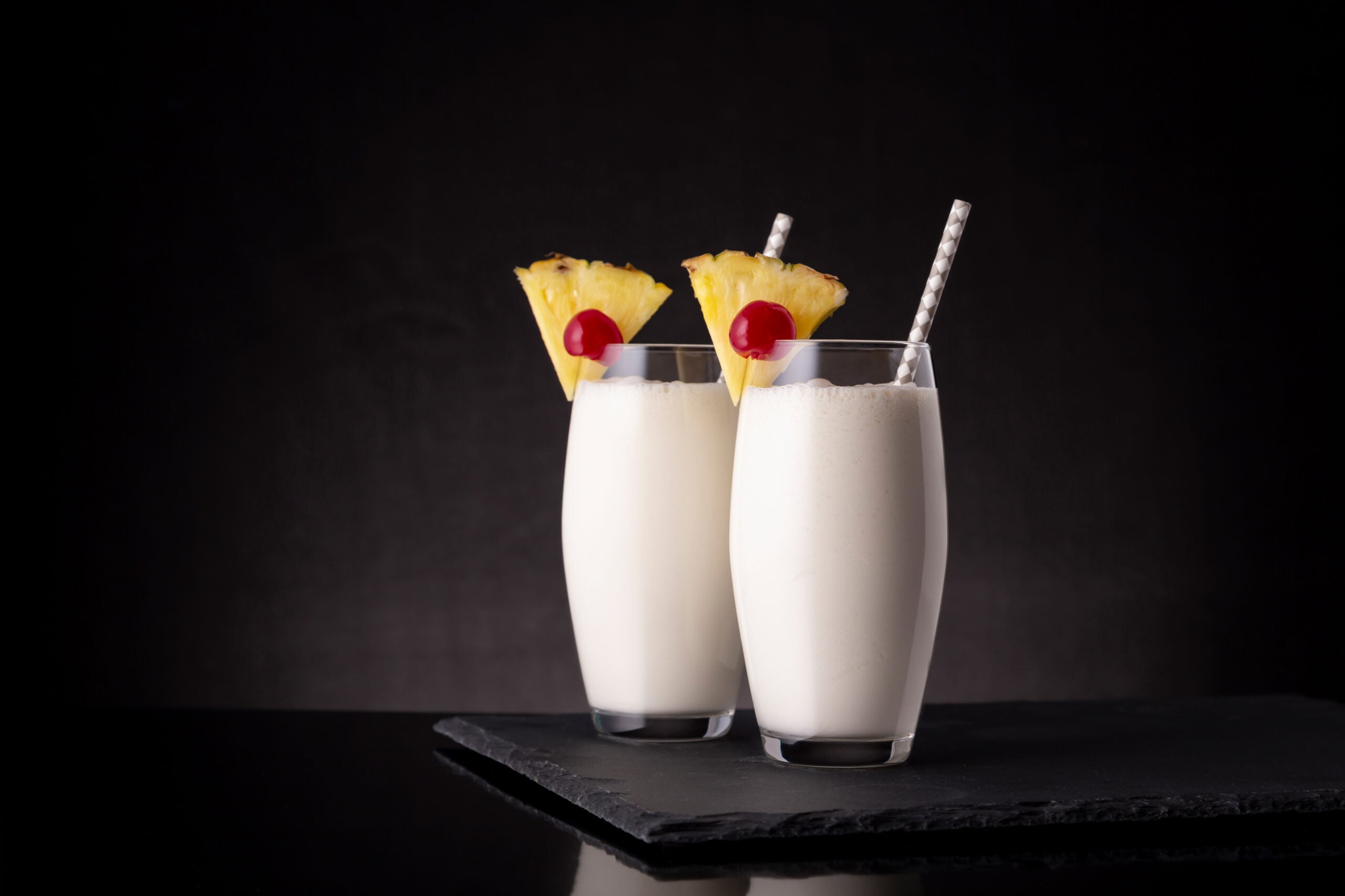 A black backdrop showcasing two piña colada mocktails. 