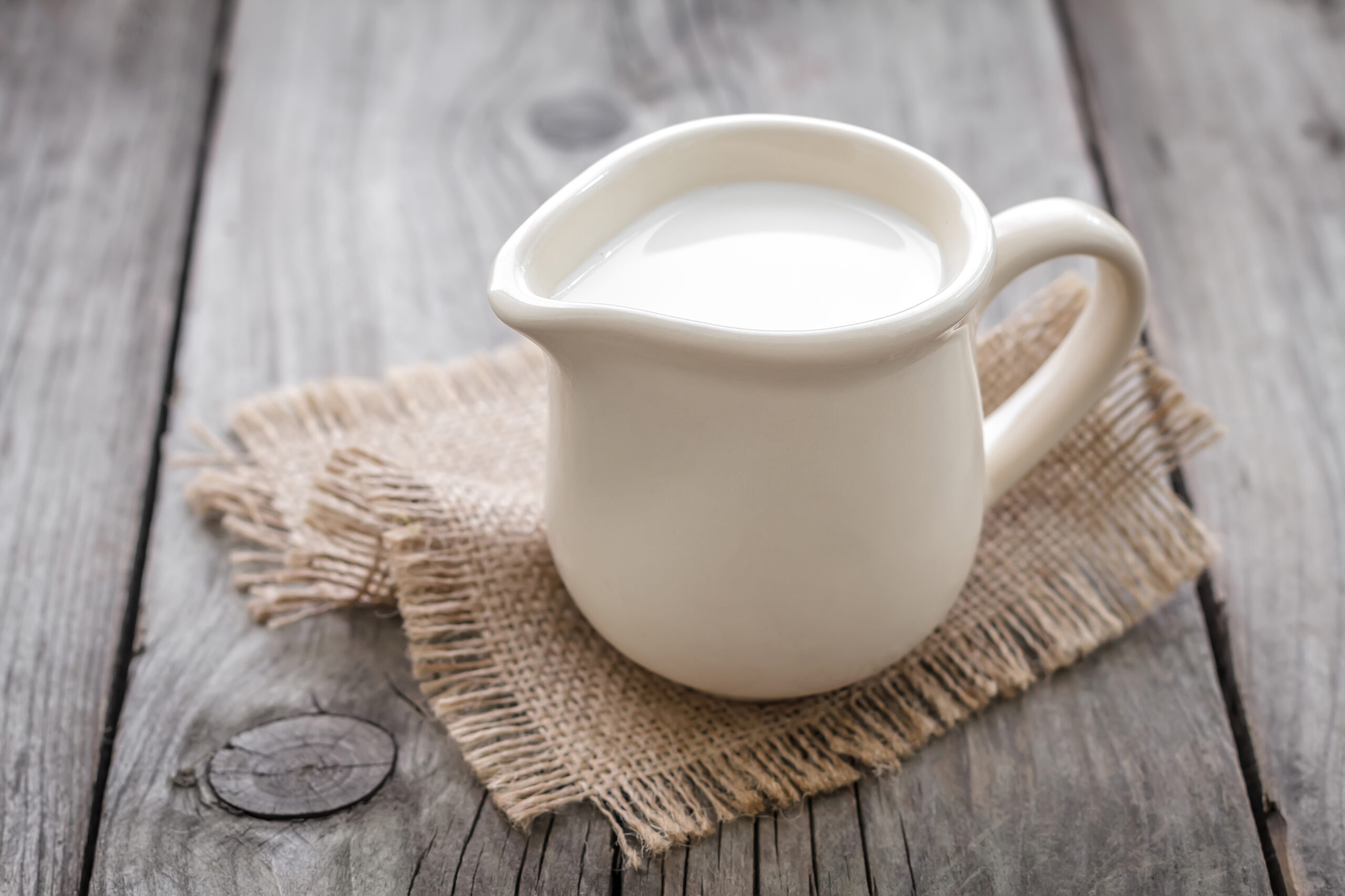 A wooden table holding a jug of fresh milk. 