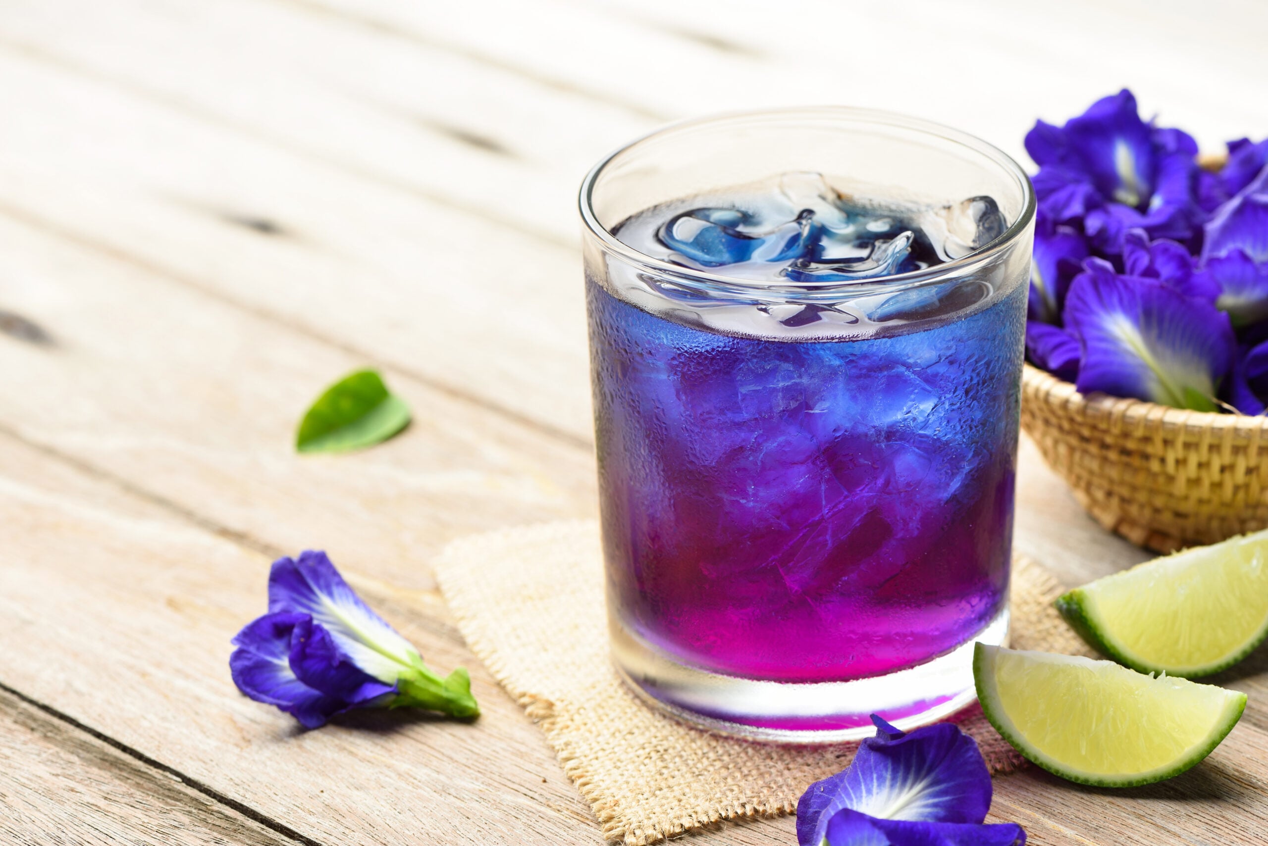 A wooden table featuring a glass of iced butterfly pea flower tea.