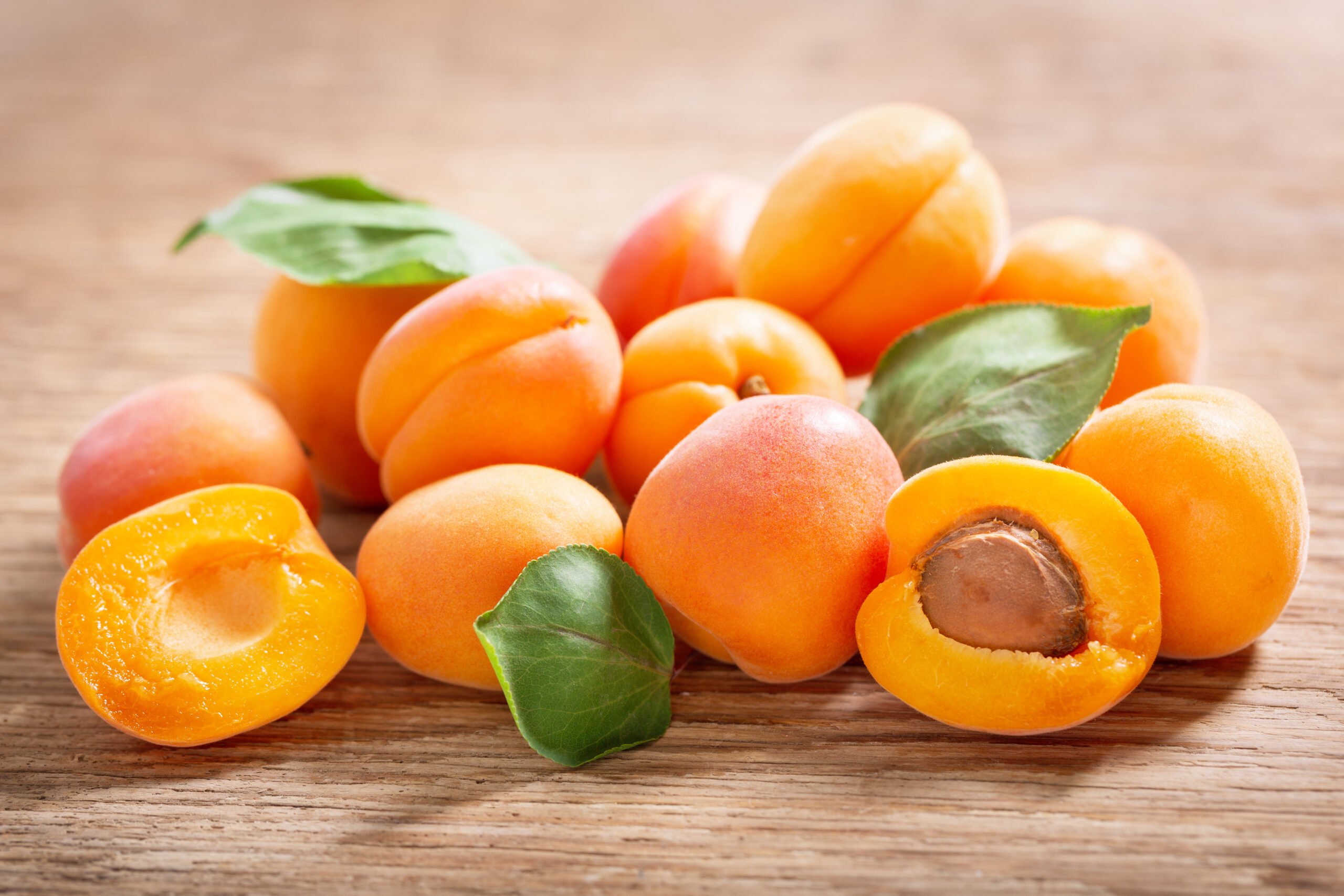 Fresh,Apricots,With,Leaves,On,A,Wooden,Table Fresh apricots resting on a wooden surface.