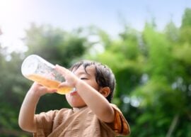 Young child drinking from a bottle outside.
