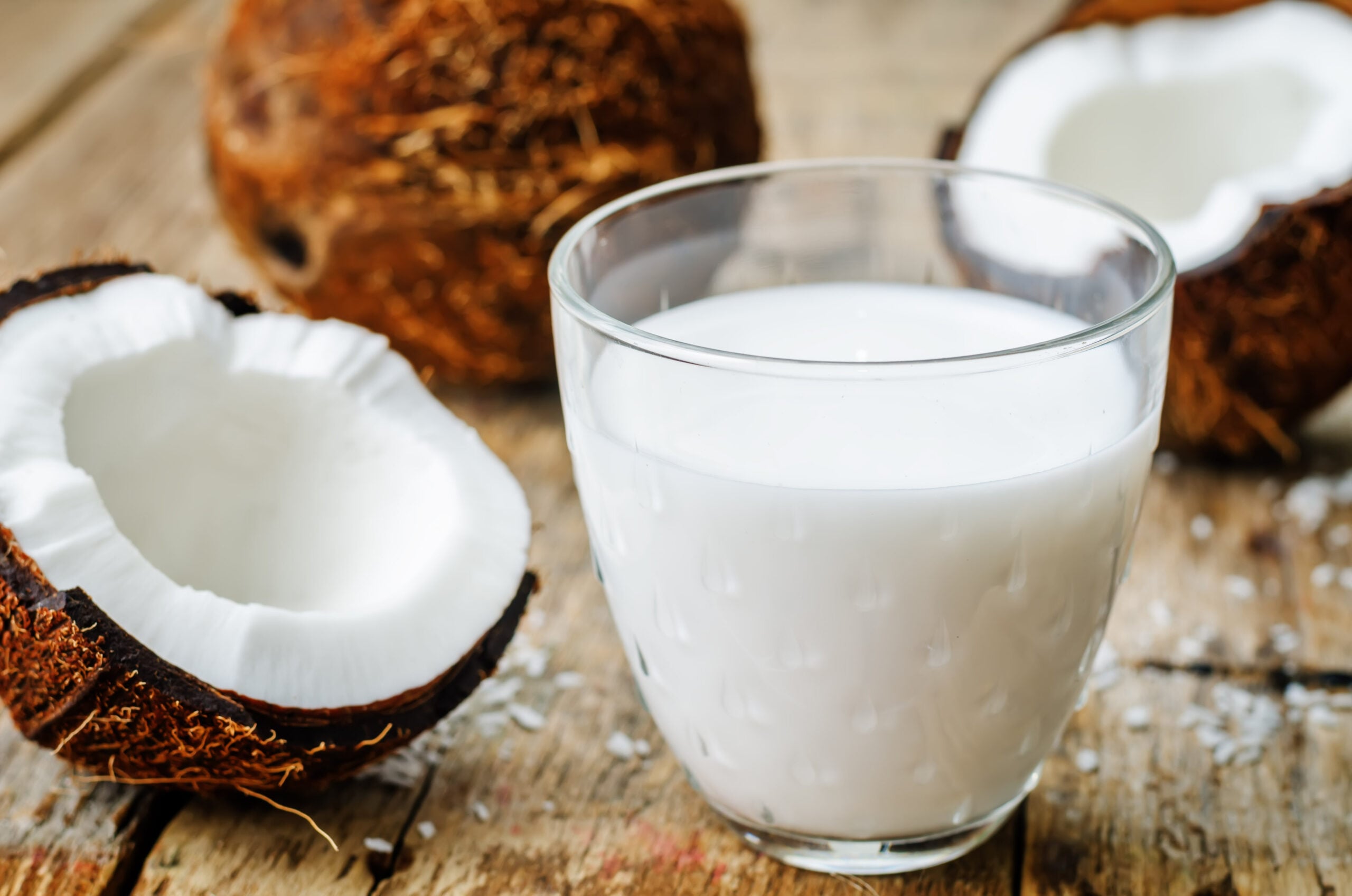 A wooden surface featuring a glass of coconut milk and some fresh coconuts.  