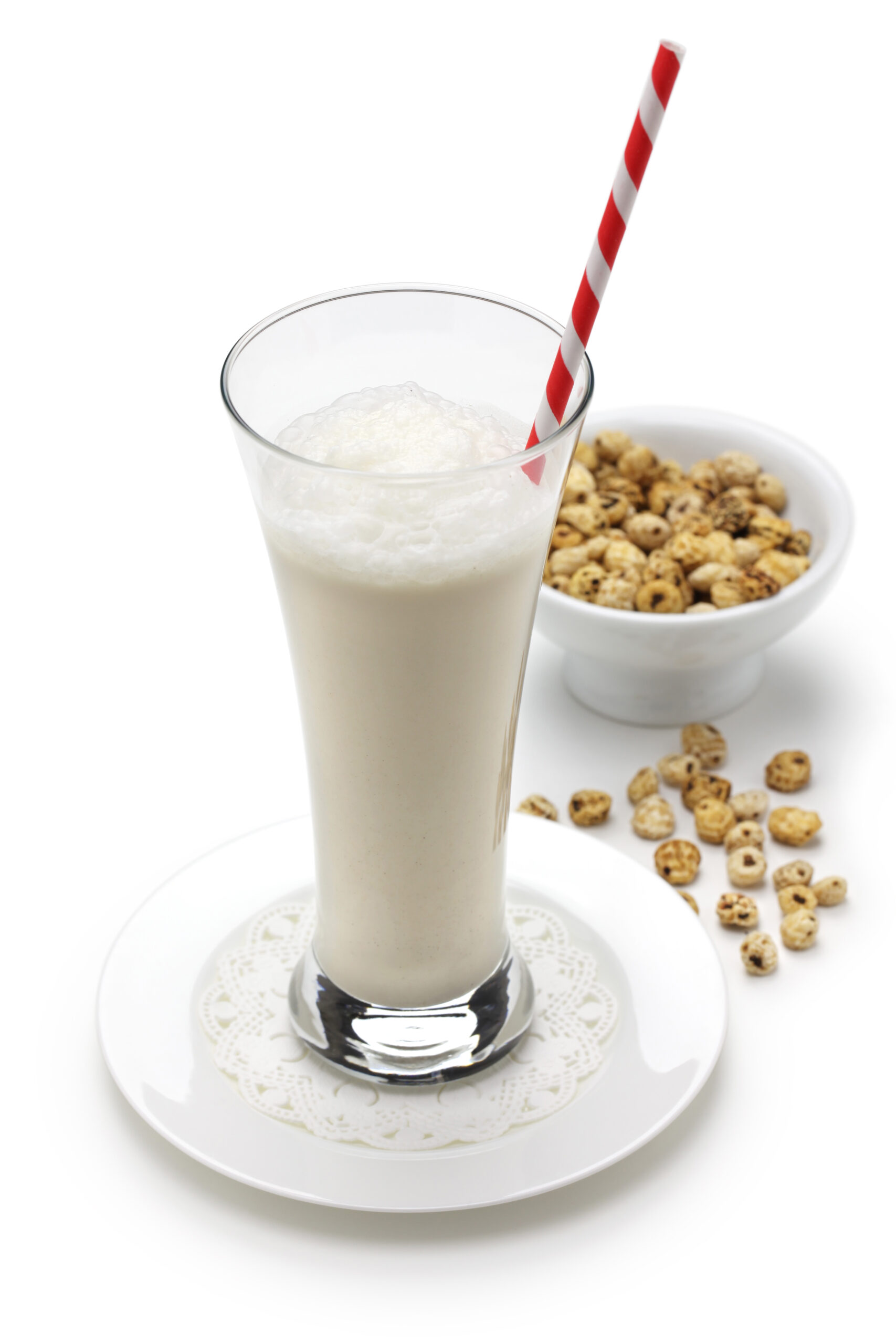 A tall glass of horchata set with a bowl overflowing with tiger nuts. 