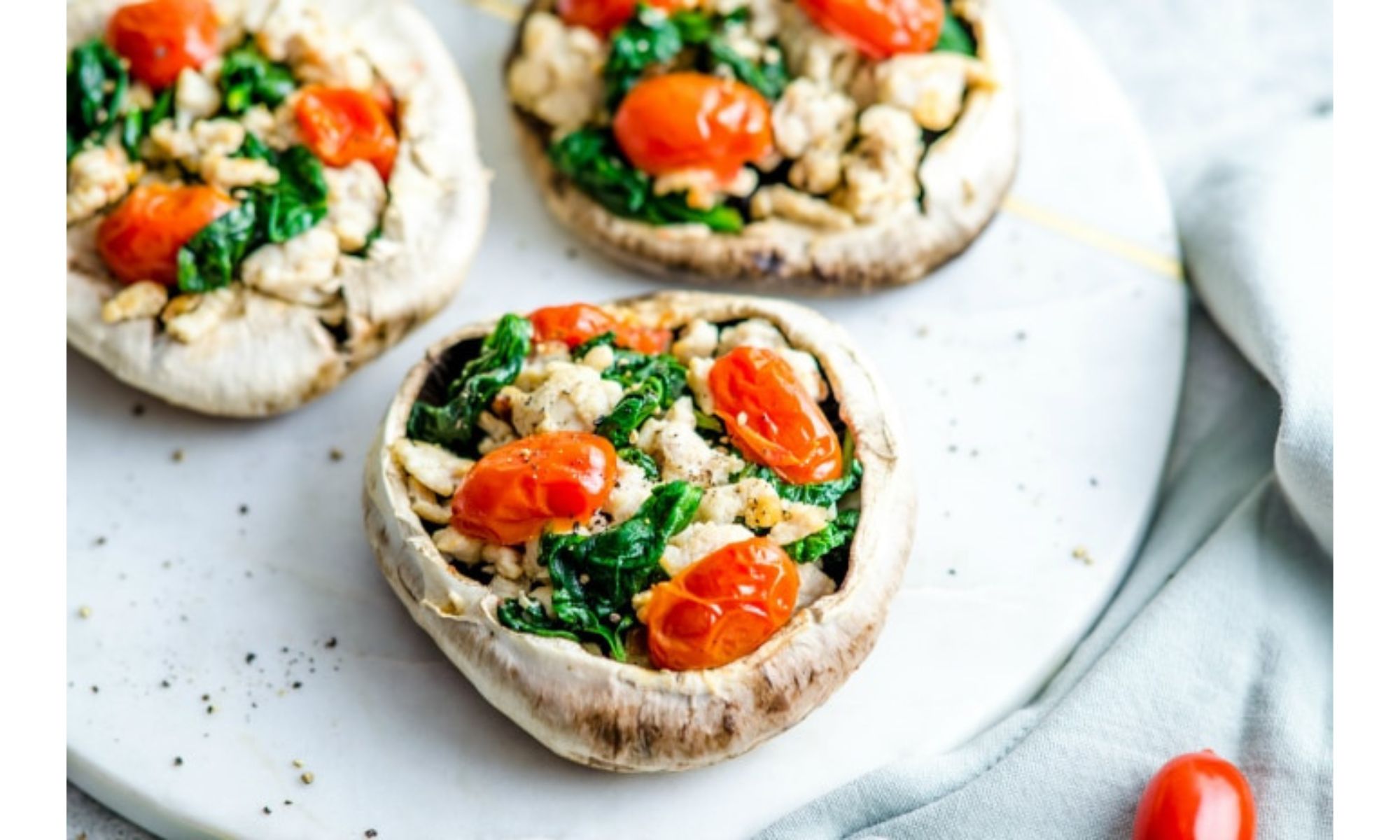 A plate of turkey stuffed portobello mushrooms with grape tomatoes and spinach.