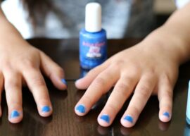 A child's hands on a table with blue painted nails next to two bottles of blue nail polish.
