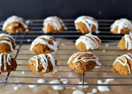 Pumpkin macarons with white chocolate drizzled over top on a cookie cooling tray.