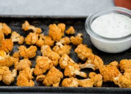 A tray of buffalo cauliflower bites beside a bowl of vegan ranch dressing.