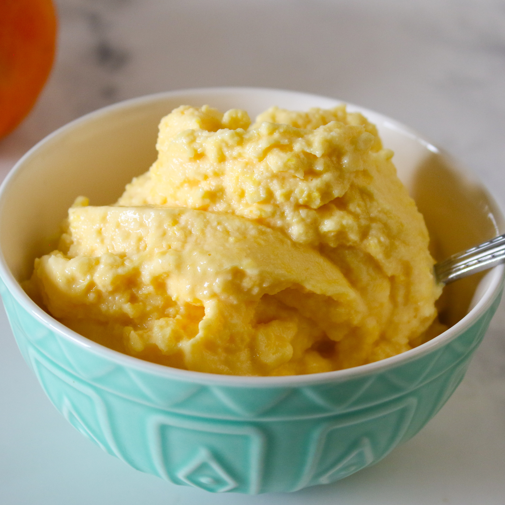 Bowl of orange sorbet on a countertop next to an orange.