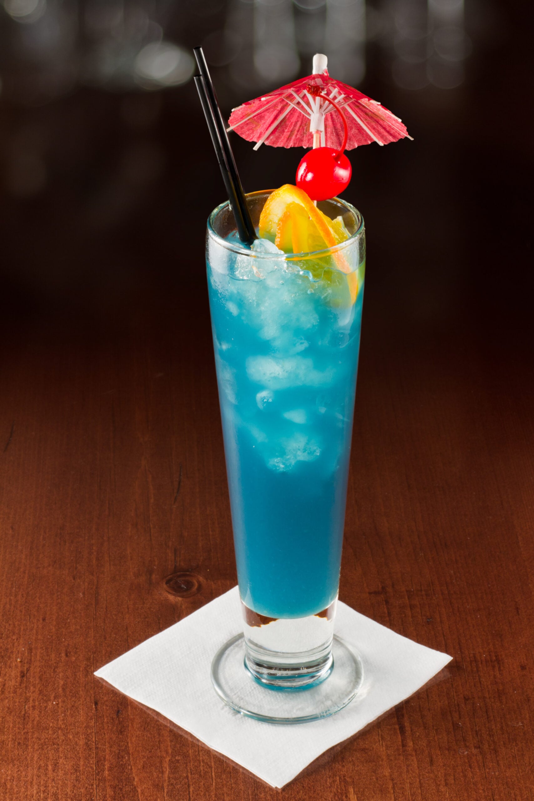 A dark backdrop featuring a tall glass full of electric lemonade. 